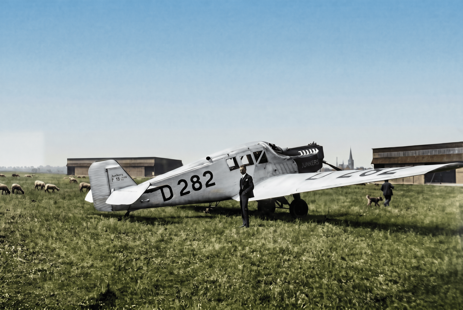 Flugzeug vor Schafherde: Die Junkers F13 auf dem Flugplatz Merzbrück. Die Konstruktion aus dem Jahr 1919 war nicht nur das erste Ganzmetallflugzeug der zivilen Luftfahrt, sondern auch das Arbeitstier der frühen Lufthansa. Ein knappes Drittel der Flugzeugflotte von 162 Maschinen im Gründungsjahr 1926 entfällt auf diesen Flugzeugtyp, insgesamt 47 Maschinen. (Foto: Archiv Forschungsflugplatz Würselen-Aachen GmbH, SW-Original und Farbversion des Bildes KI-bearbeitet)