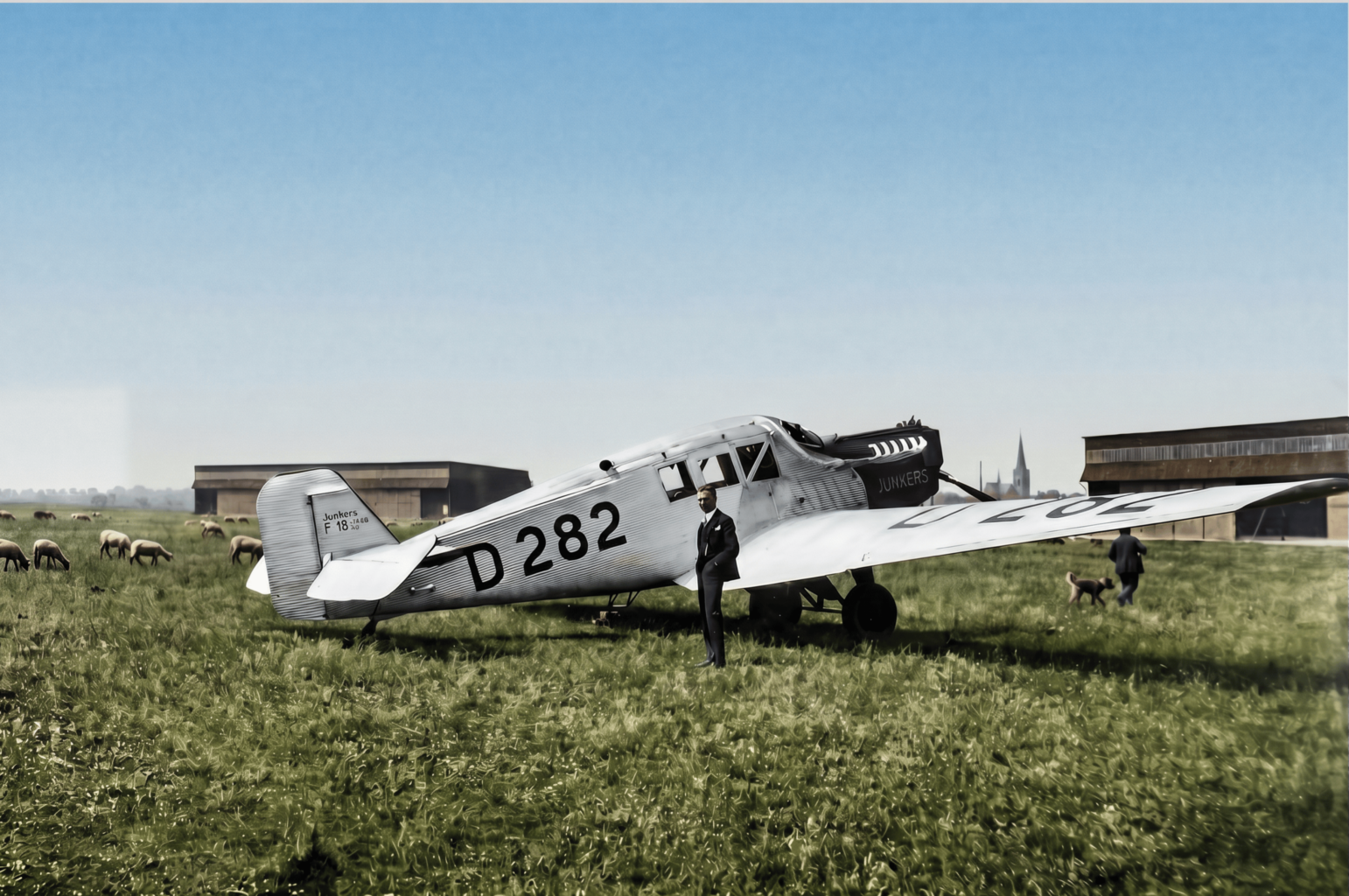 Flugzeug vor Schafherde: Die Junkers F13 auf dem Flugplatz Merzbrück. Die Konstruktion aus dem Jahr 1919 war nicht nur das erste Ganzmetallflugzeug der zivilen Luftfahrt, sondern auch das Arbeitstier der frühen Lufthansa. Ein knappes Drittel der Flugzeugflotte von 162 Maschinen im Gründungsjahr 1926 entfällt auf diesen Flugzeugtyp, insgesamt 47 Maschinen. (Foto: Archiv Forschungsflugplatz Würselen-Aachen GmbH, SW-Original und Farbversion des Bildes KI-bearbeitet)