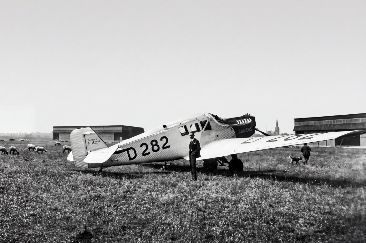 Flugzeug vor Schafherde: Die Junkers F13 auf dem Flugplatz Merzbrück. Die Konstruktion aus dem Jahr 1919 war nicht nur das erste Ganzmetallflugzeug der zivilen Luftfahrt, sondern auch das Arbeitstier der frühen Lufthansa. Ein knappes Drittel der Flugzeugflotte von 162 Maschinen im Gründungsjahr 1926 entfällt auf diesen Flugzeugtyp, insgesamt 47 Maschinen. (Foto: Archiv Forschungsflugplatz Würselen-Aachen GmbH, SW-Original und Farbversion des Bildes KI-bearbeitet)