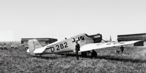 Flugzeug vor Schafherde: Die Junkers F13 auf dem Flugplatz Merzbrück. Die Konstruktion aus dem Jahr 1919 war nicht nur das erste Ganzmetallflugzeug der zivilen Luftfahrt, sondern auch das Arbeitstier der frühen Lufthansa. Ein knappes Drittel der Flugzeugflotte von 162 Maschinen im Gründungsjahr 1926 entfällt auf diesen Flugzeugtyp, insgesamt 47 Maschinen. (Foto: Archiv Forschungsflugplatz Würselen-Aachen GmbH, SW-Original und Farbversion des Bildes KI-bearbeitet)