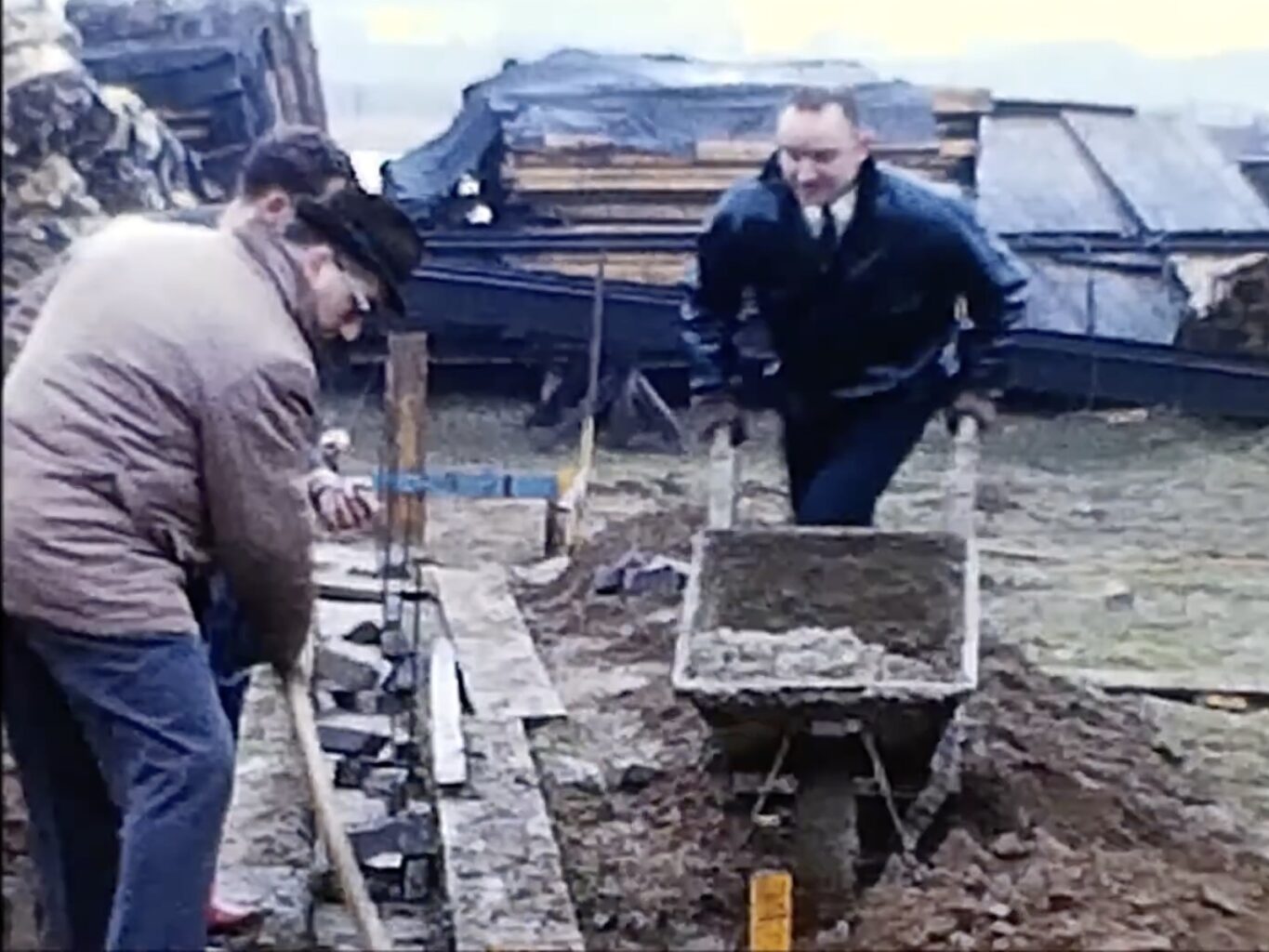 Eine solide Grundlage ist die Basis für ein gutes Fundament (oder so ähnlich): An der Schubkarre Joschi Stelzen, mit Schaufel: Peter Leuchter, im Hintergrund: Klaus Engels (Foto: Luftsportverein Aachen e.V. Film-Original und restaurierte Fassung mit KI-Unterstützung bearbeitet)