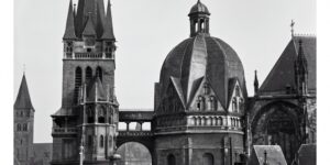 Eine schwebende Sensation: Das Luftschiff "Graf Zeppelin" über dem Dom von Aachen. Unten rechts Zuschauer auf Häuserdächern (Foto: Forschungsflugplatz Würselen-Aachen GmbH, SW-Original und Farbversion des Bildes mit KI-Unterstützung restauriert und koloriert)